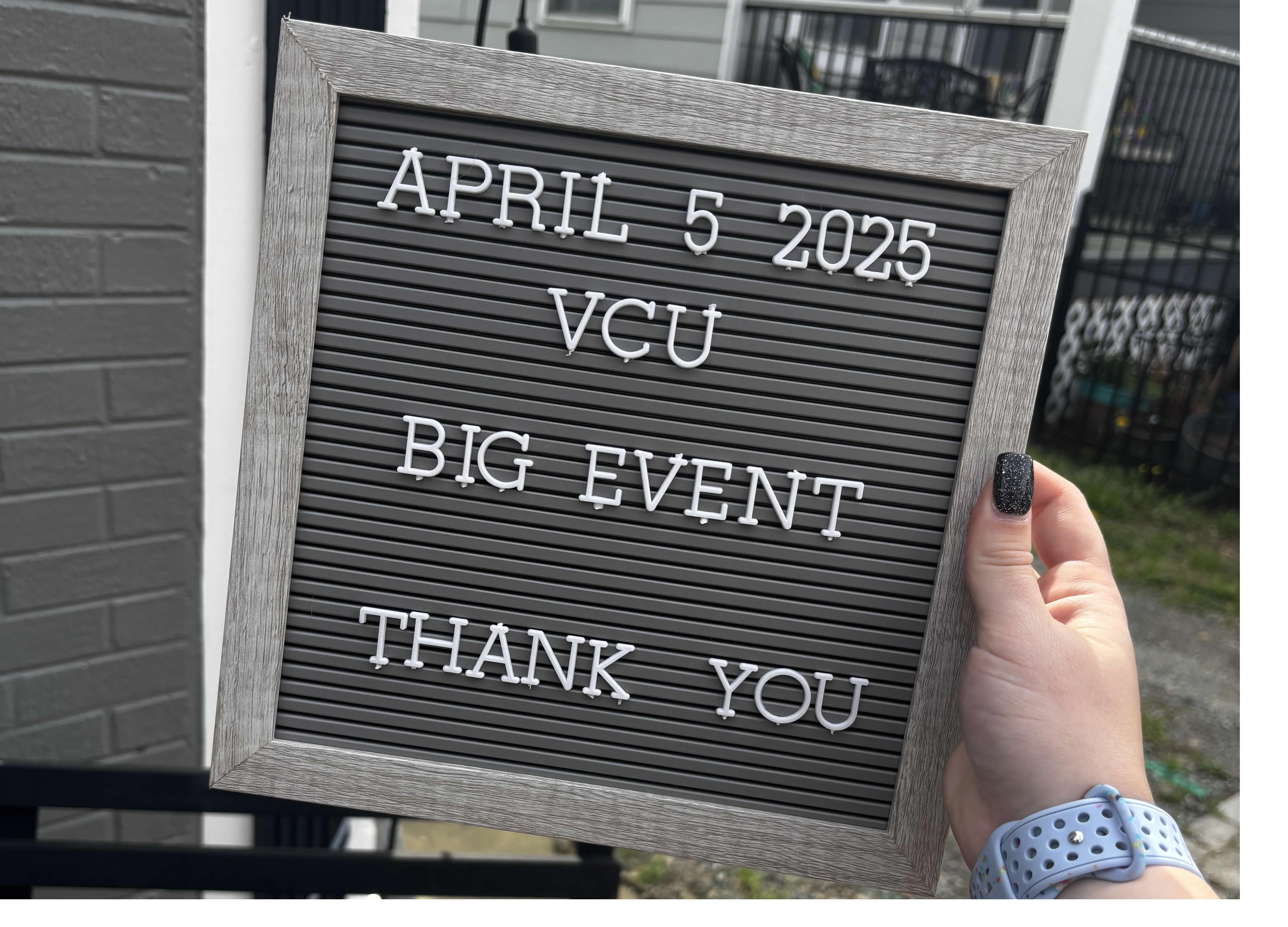 Hand holds a board reading “April 5 2025 VCU Big Event Thank You” in front of a house.