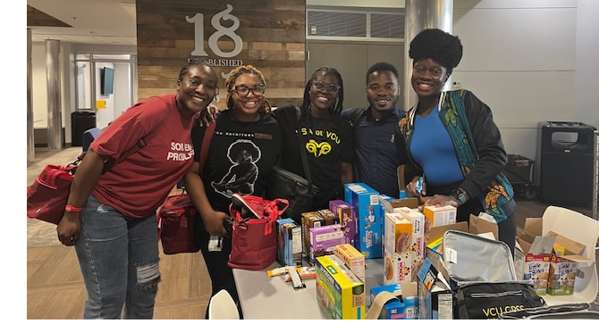 A group of five GPSS students smiles behind a table filled with snacks and pantry items.